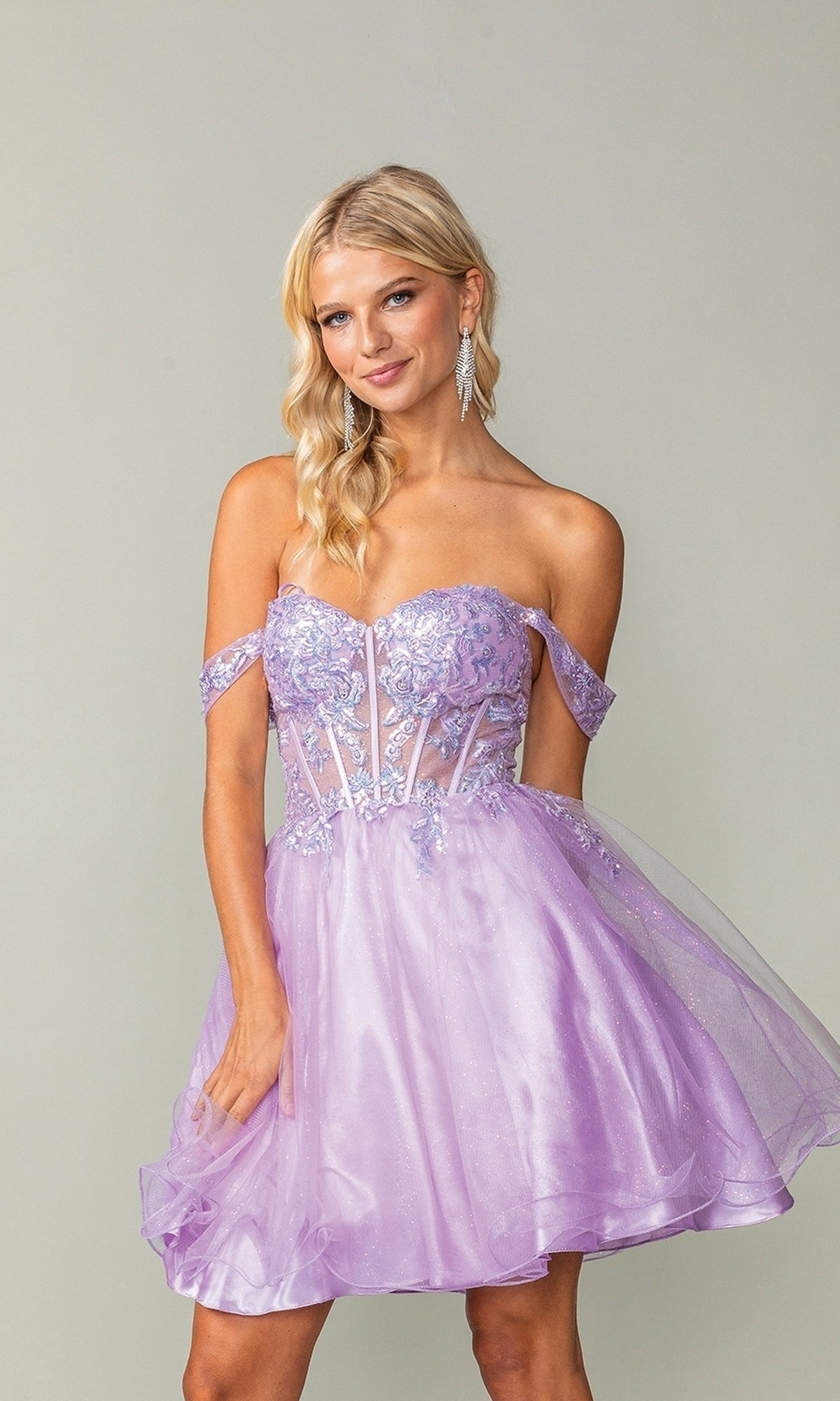A woman stands against a plain background wearing the Dancing Queen 3383 short corset homecoming dress featuring a sparkly sheer bodice and floral embroidery.
